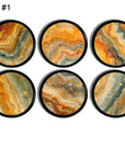 Set of six handmade cabinet knobs with vibrant, marble like patterns on a round, black base. Unique drawer pulls featuring unique swirling designs in rich shades of orange, yellow, blue, and brown, giving an artistic and natural stone formation inspired aesthetic.