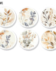 Six-piece neutral botanical cabinet knob and drawer pull collection featuring soft watercolor leaves in beige, sage, gray, and warm earth tones on white knob bases, ideal for organic modern, Scandinavian, and contemporary furniture makeovers
