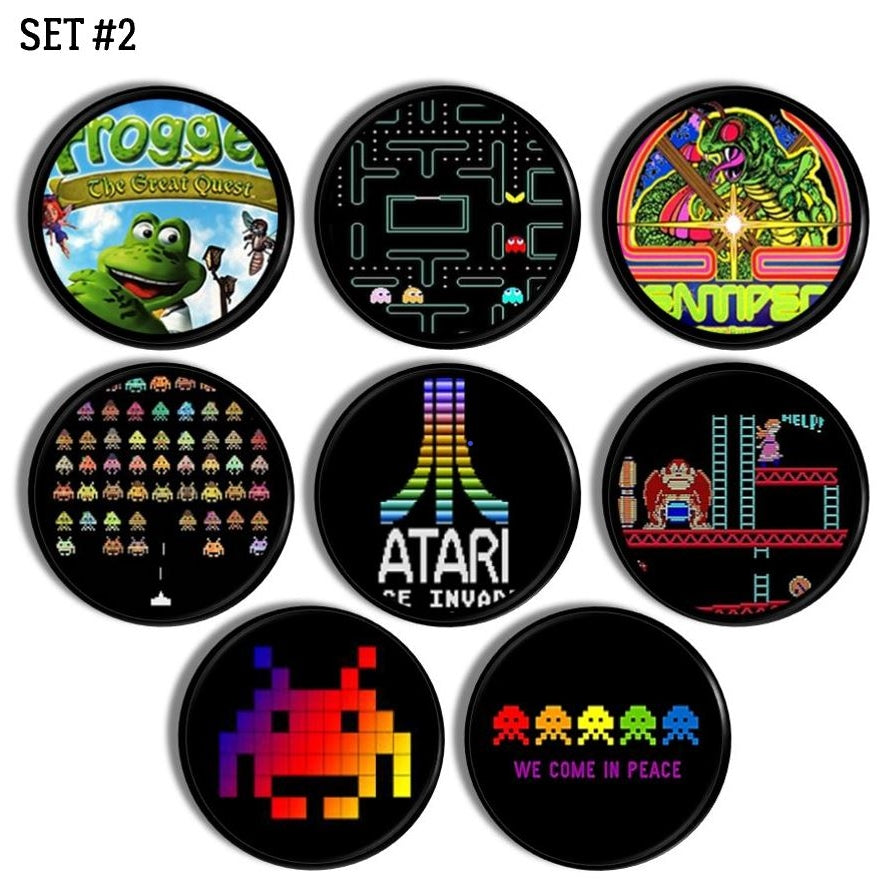 Eight black knobs featuring colorful retro arcade game artwork. Includes Frogger, Pac‑Man, Centipede, Space Invaders, Donkey Kong, Atari logo, pixel aliens, and colorful ghost characters. Handcrafted drawer pulls for gamer pad or entertainment center.