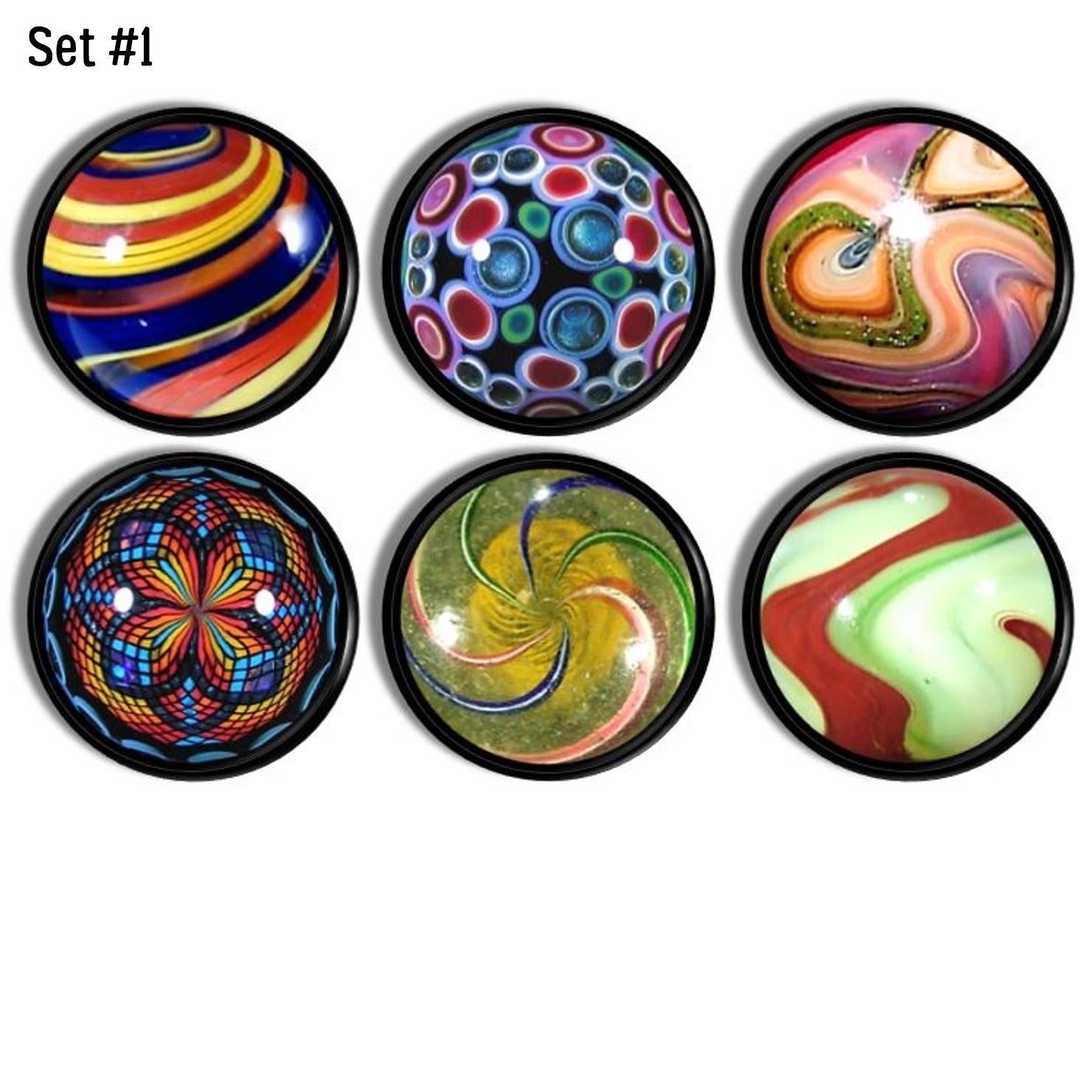 Six handcrafted cabinet drawer pulls featuring simulated vintage glass marble designs on a black base knob, with bold spirals, kaleidoscope bursts, glitter accents, and multicolor swirls inspired by classic retro toy marbles.